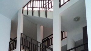 Un intérieur à plusieurs niveaux, avec un escalier central entouré de murs blancs et de rampes en bois foncé.
