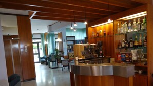 En hotellobby med en receptionsdisk i trä, en kaffemaskin och en bardisk med ett urval av olika flaskor.