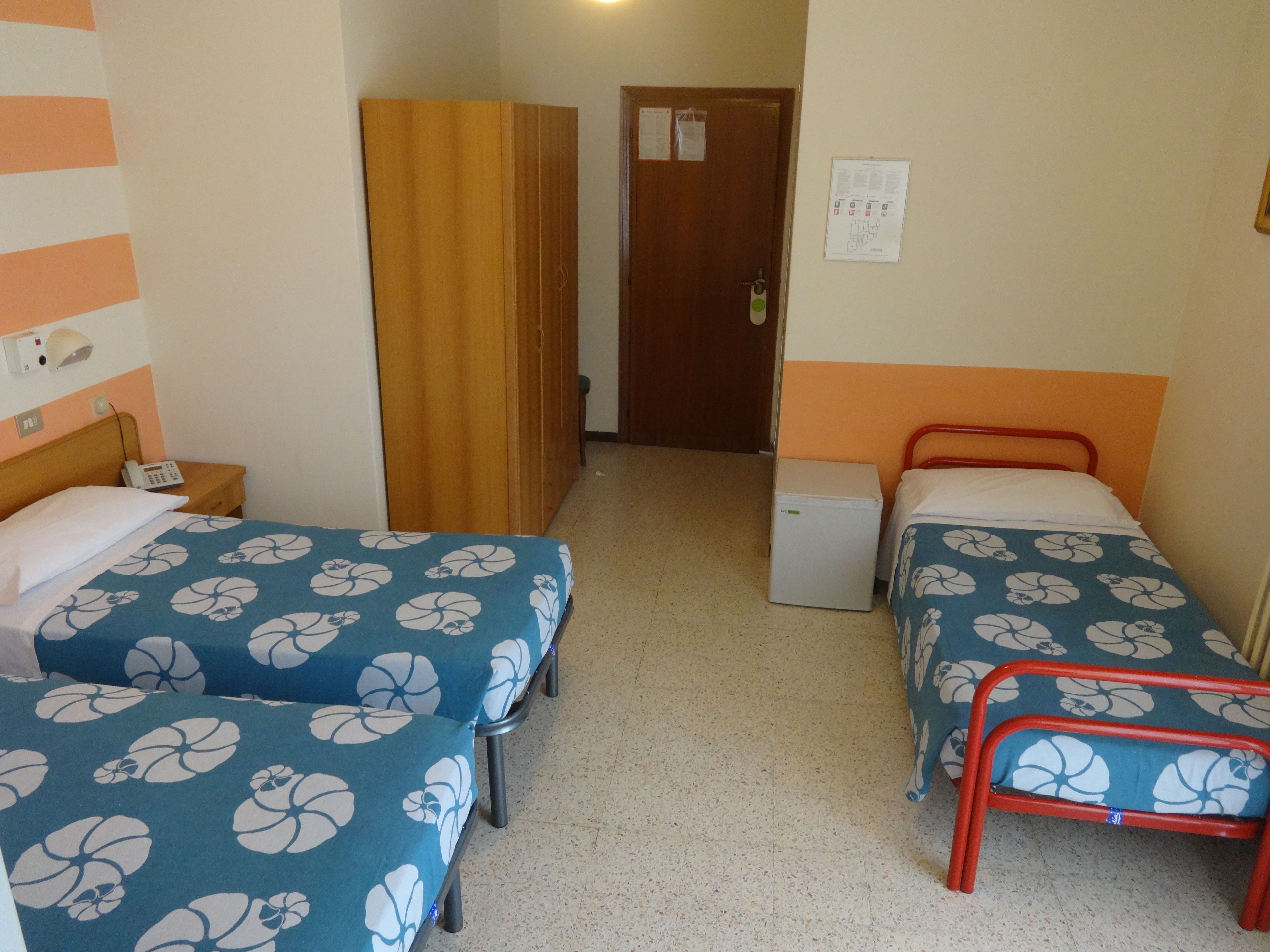 A hotel room with two beds, a wardrobe, a small fridge, and a desk with a phone.