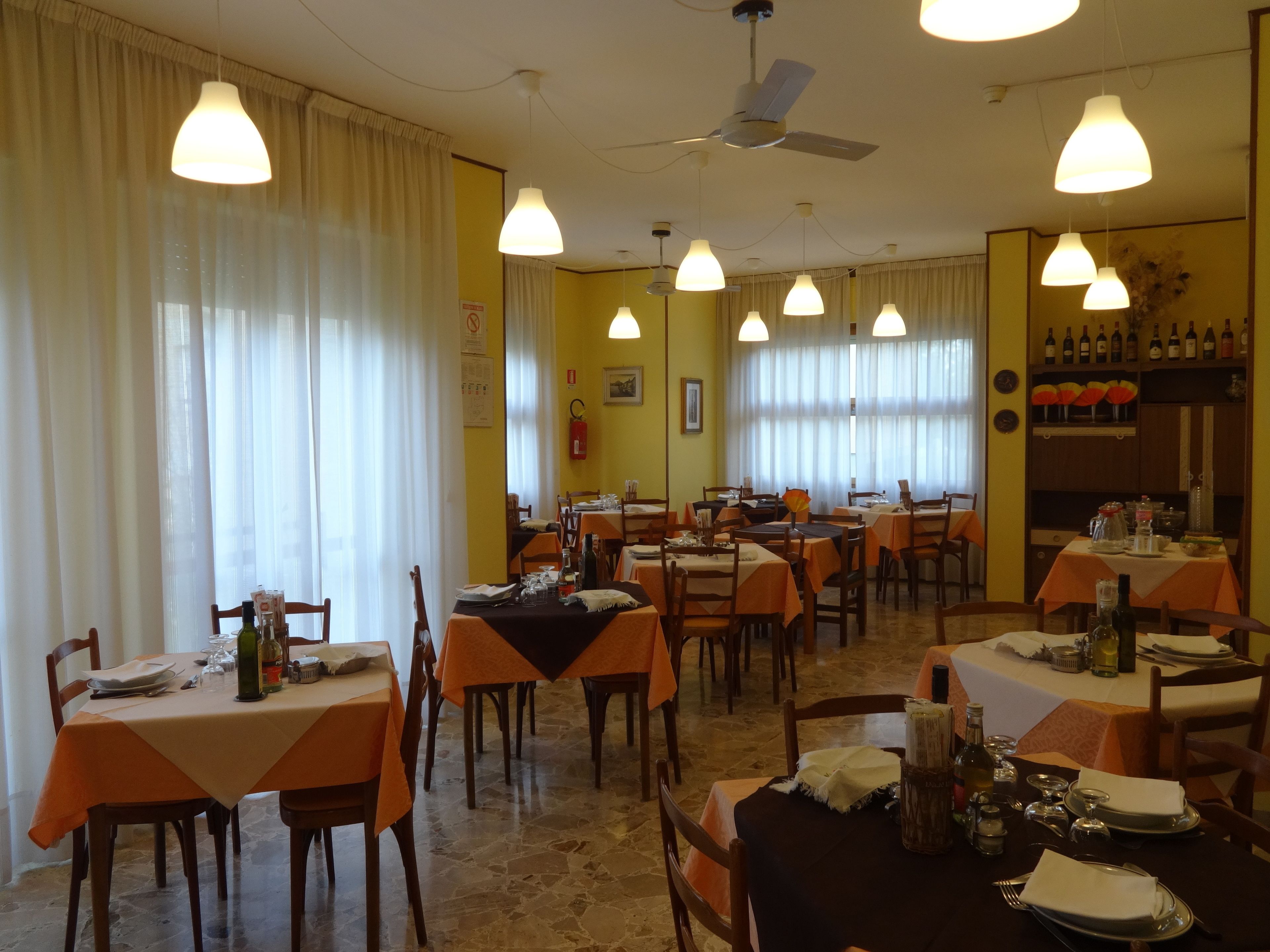 Zona pranzo con diversi tavoli, sedie e lampadari a sospensione.