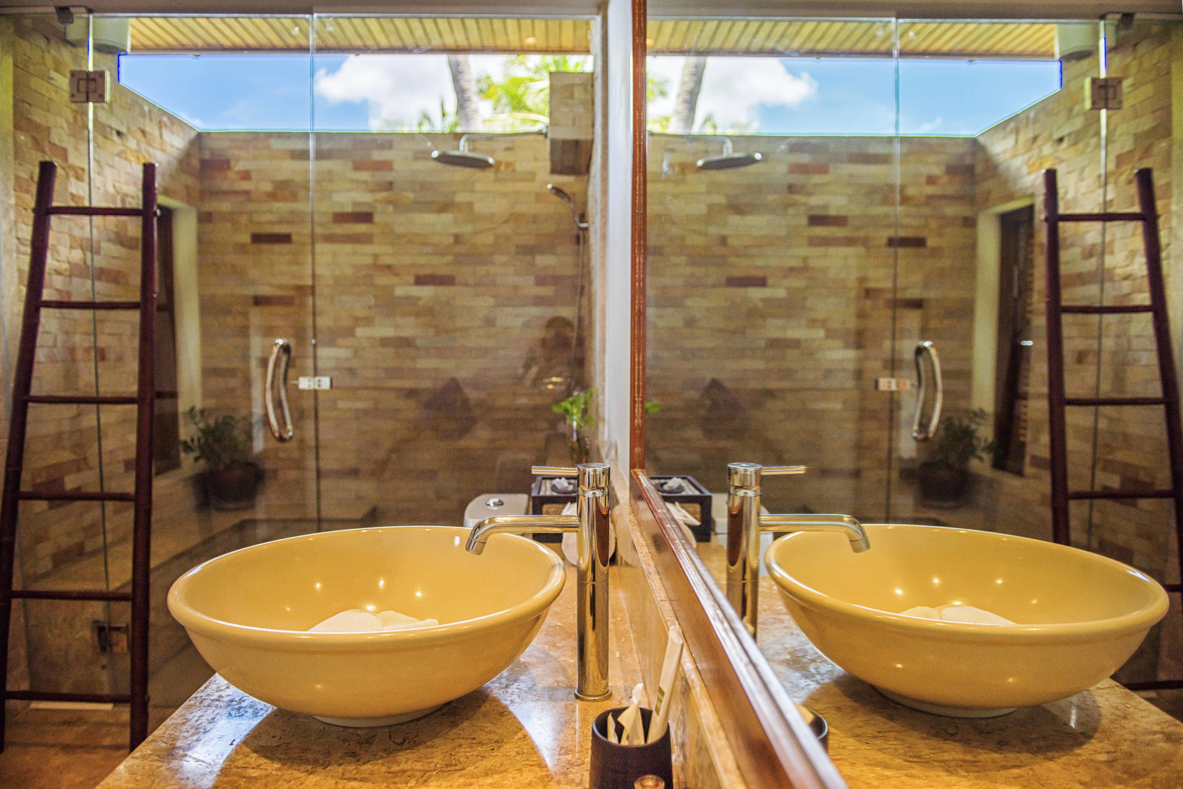 A bathroom with two yellow sinks, a glass shower enclosure, and a view of the sky through the shower door.