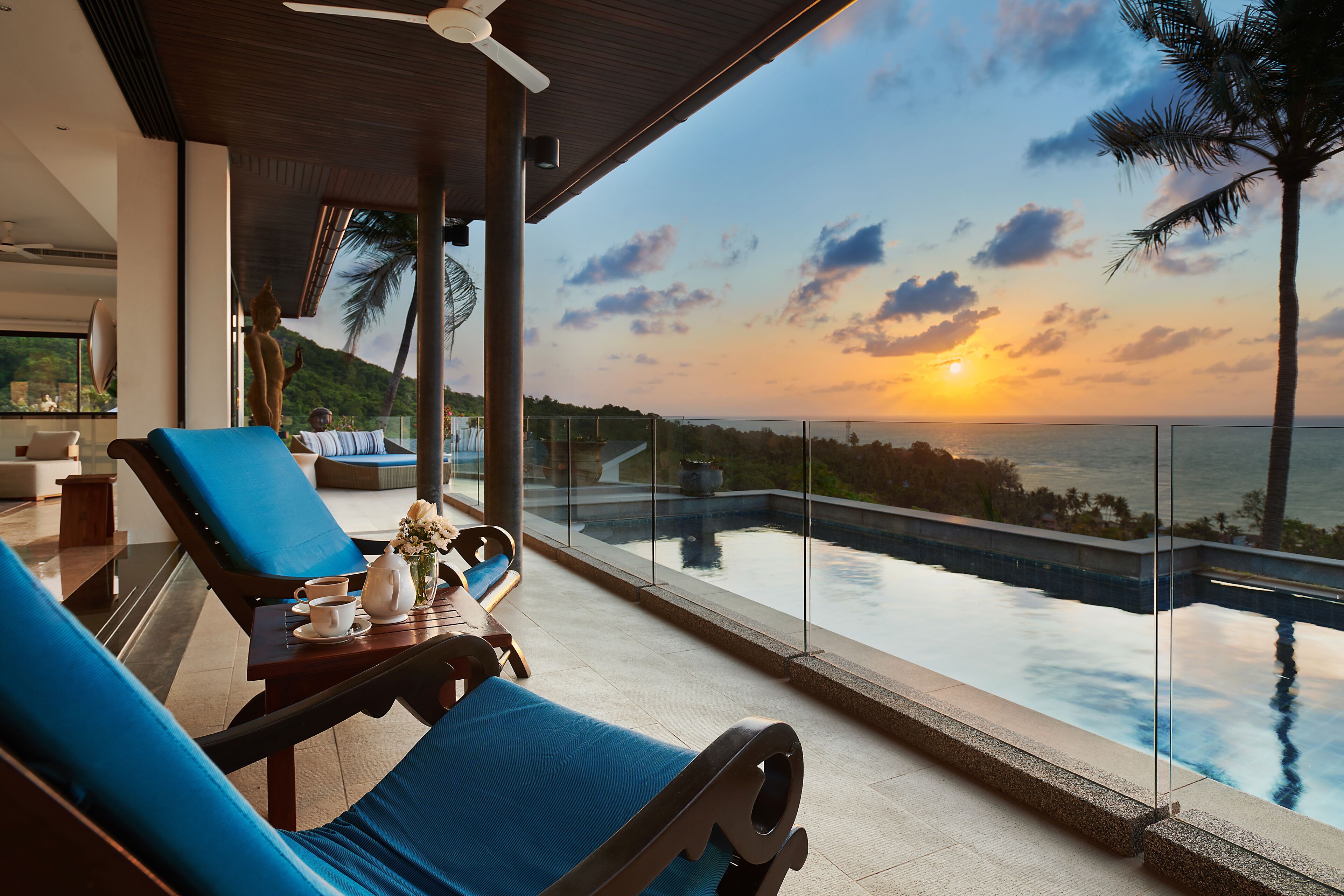 A modern lounge with a view of the sunset over the ocean, a pool, and a palm tree.
