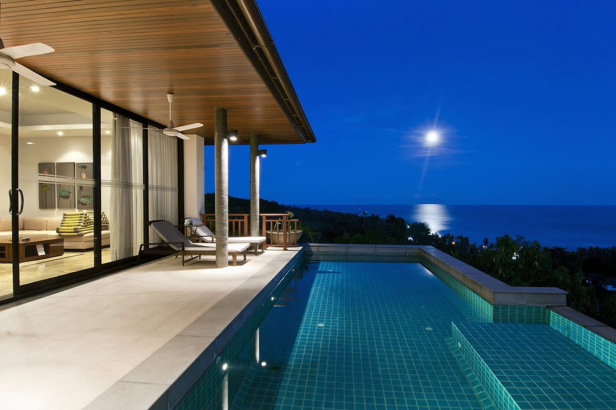 Zona de piscina exterior moderna con vista al océano al atardecer.