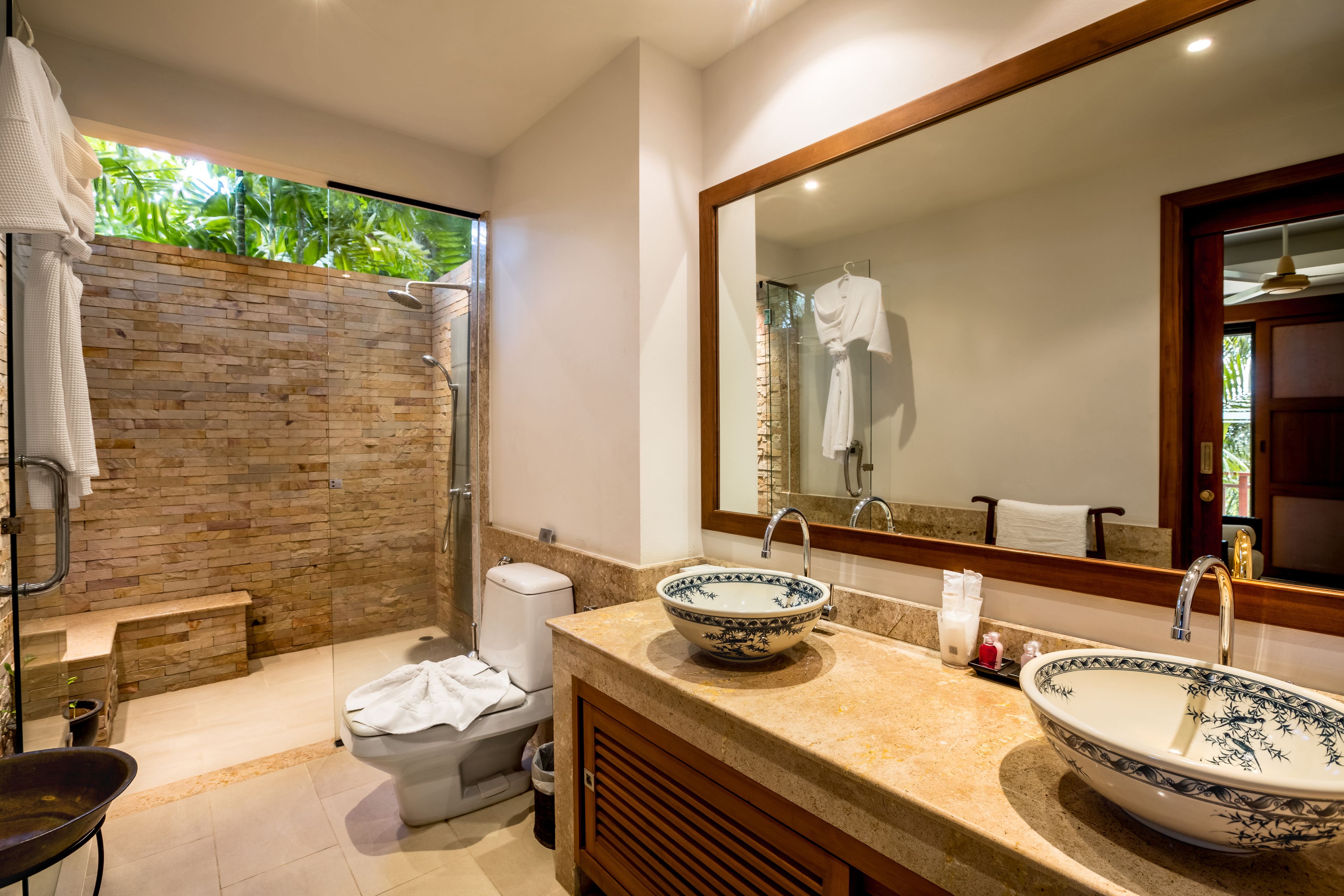 Un baño moderno con ducha de mampara de vidrio, un espejo grande y dos lavamanos con cuencos decorativos.