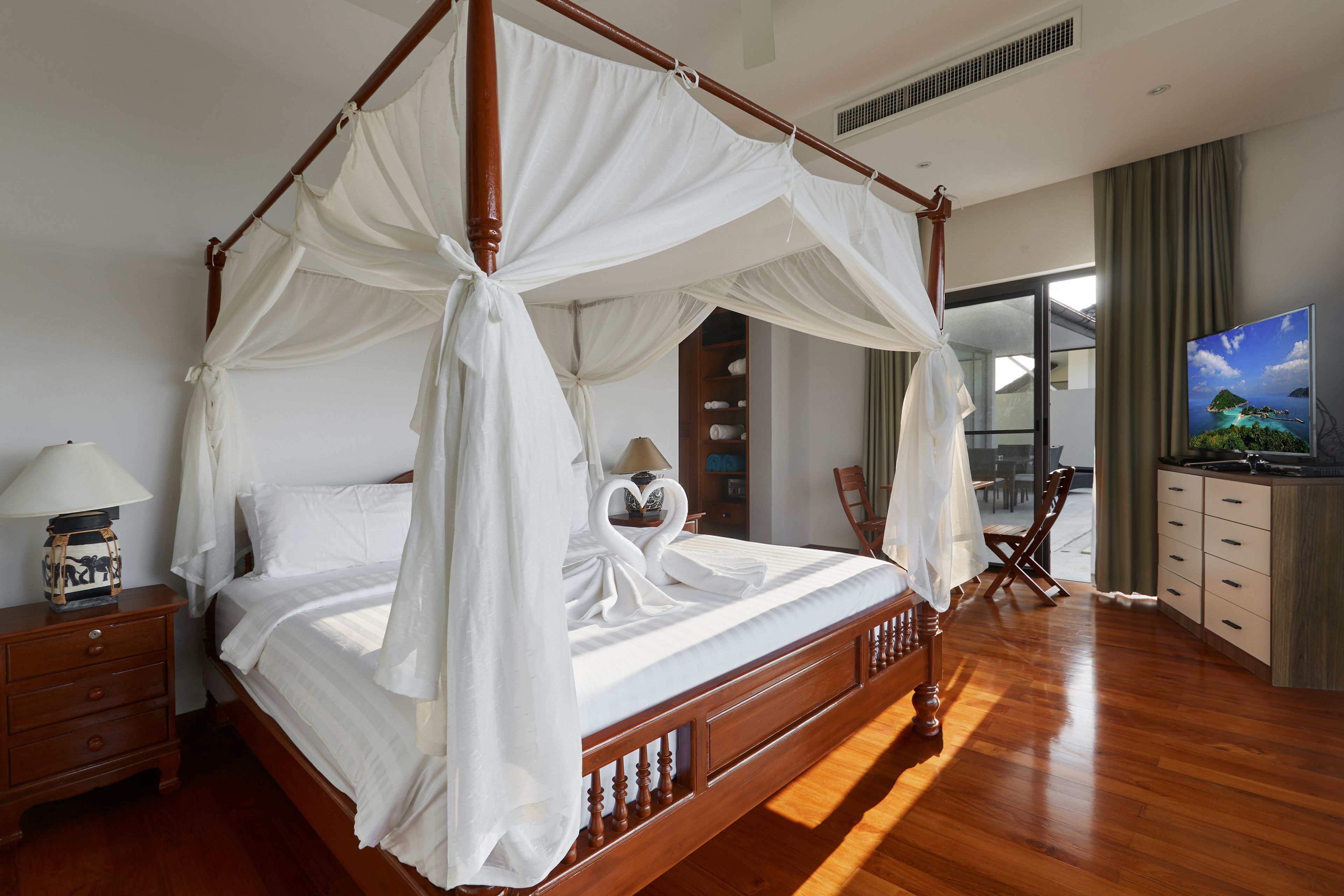 A four-poster bed with a canopy, wooden nightstands, a television, and a view of the ocean through a window.