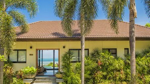 A two-story house with a tiled roof, a large glass door leading to a balcony, and a well-maintained garden with various plants and a small pool. - Villa Baan Saitara (Koh Samui)