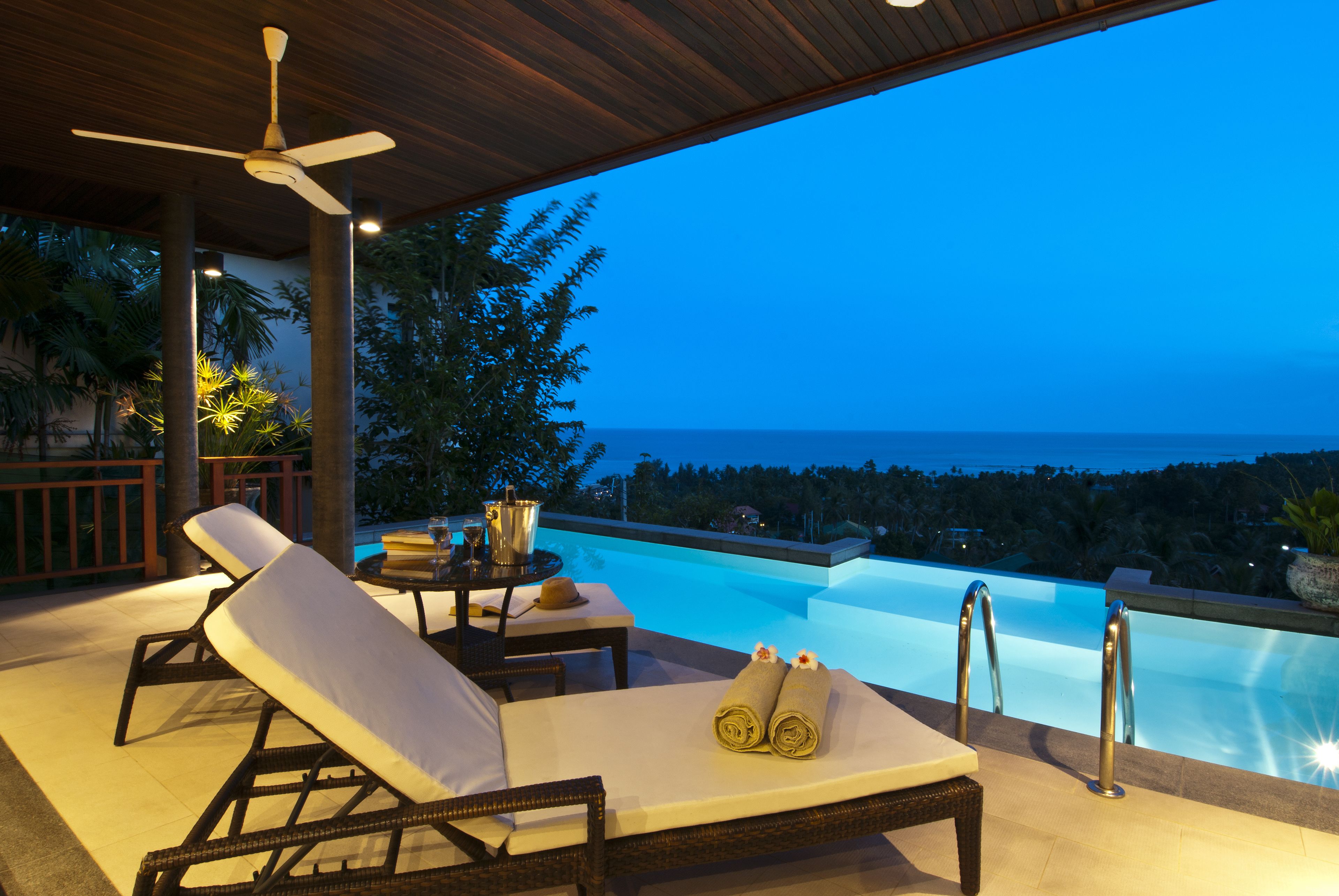 Eine Poollounge mit Liegestühlen, einem Tisch mit einem Getränk und Blick auf das Meer im Abenddämmerung.