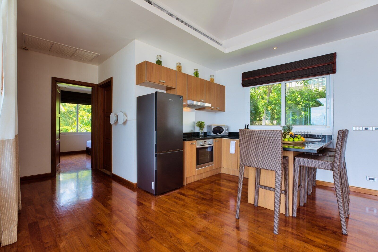 A modern kitchen with wooden cabinets, a black refrigerator, and a dining area with wicker chairs.