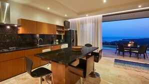 A modern kitchen with a central island, bar stools, and a dining area with a view. - Villa Baan Saitara (Koh Samui)