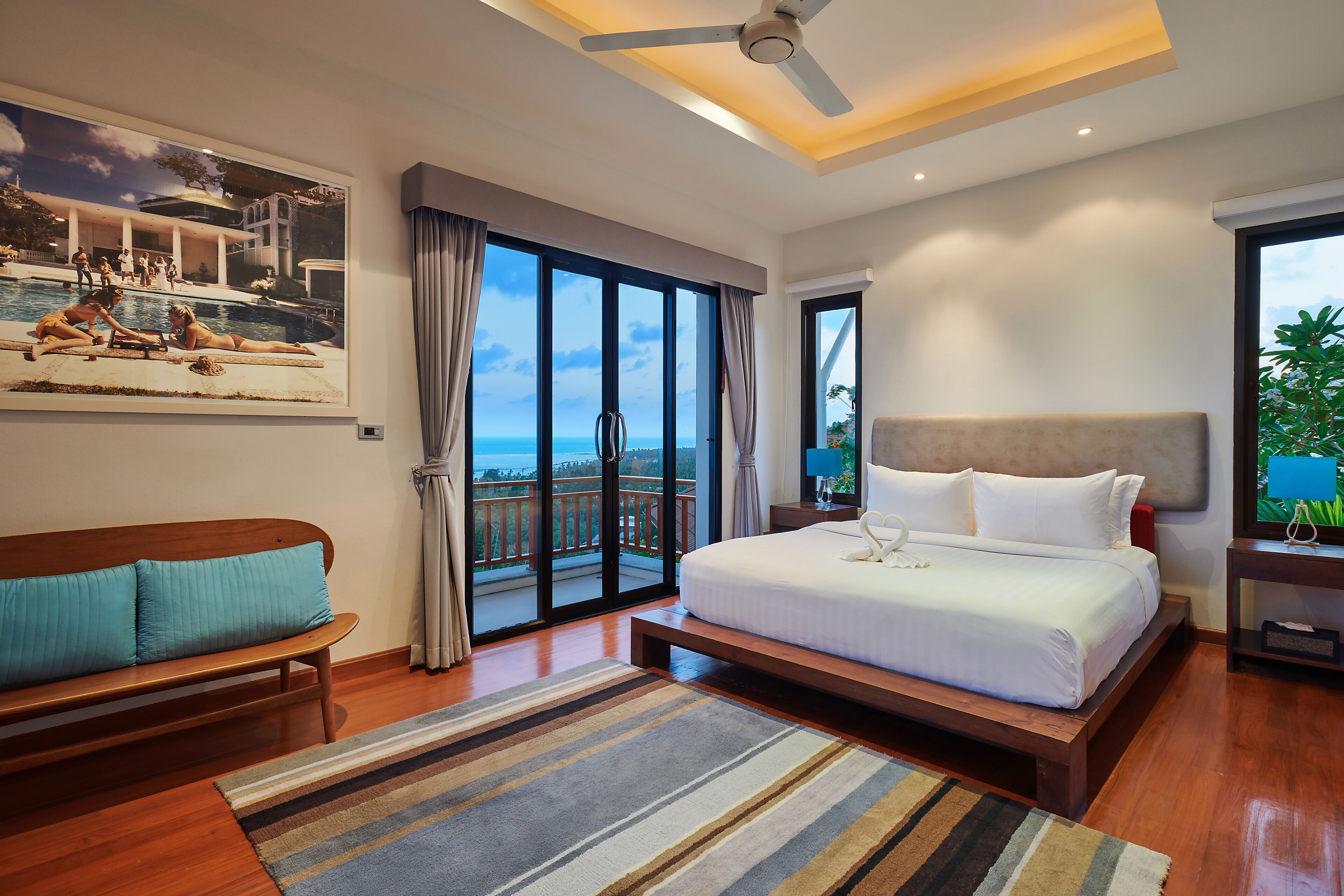 A hotel room with a large bed, a bench, a view of the pool, and a ceiling fan.