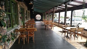 Ein Restaurant mit überdachter Außenbestuhlung, Steinmauern und Blick auf die Straße.