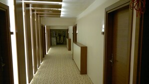 Ein Hotelgang mit gemustertem Teppich, Holztüren und einer Deckenleuchte.