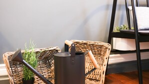 Een rieten stoel met een kussen, een metalen pot en een tuingereedschap.