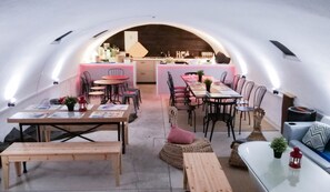 Una zona d'esmorzar amb arc, amb taules i cadires, una cuina al fons i una zona d'estar acollidora amb coixins.