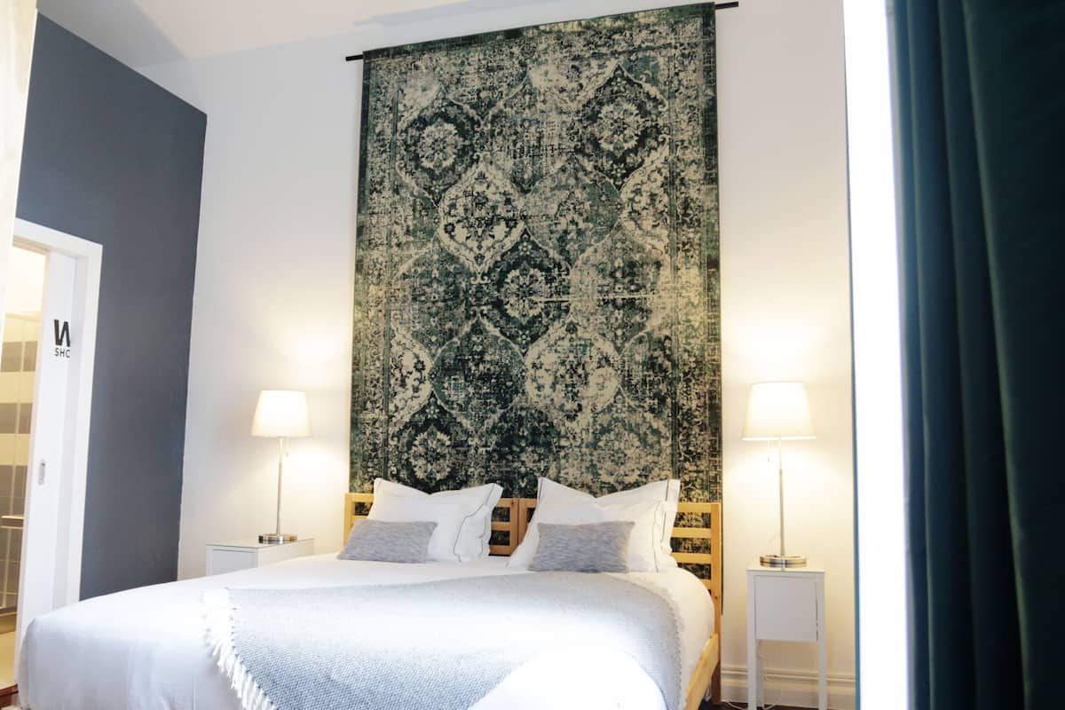 A hotel room with a large bed, two bedside tables, a wall tapestry, and a door with a sign.