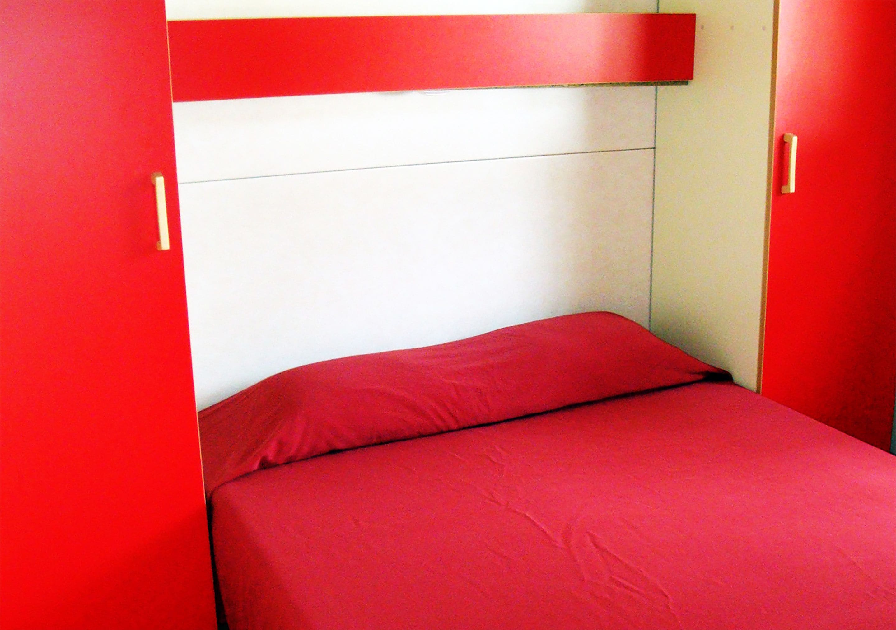 A small, red-framed bed with a white headboard in a room with red walls.