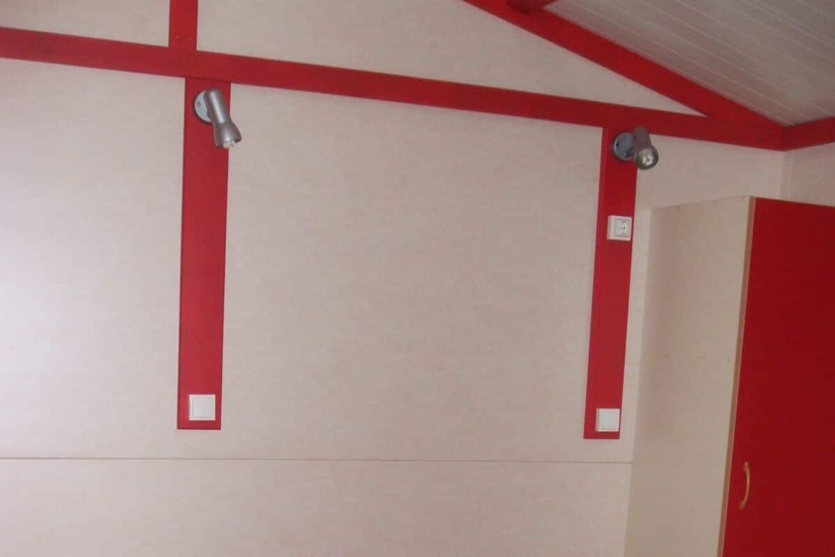 A single bed with a red bedspread in a room with white walls and red trim.
