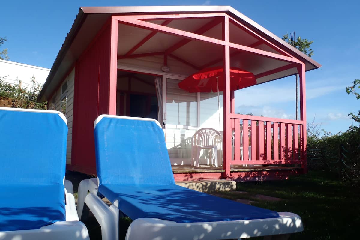 A small red building with a covered porch, two blue lounge chairs, and a table with chairs.