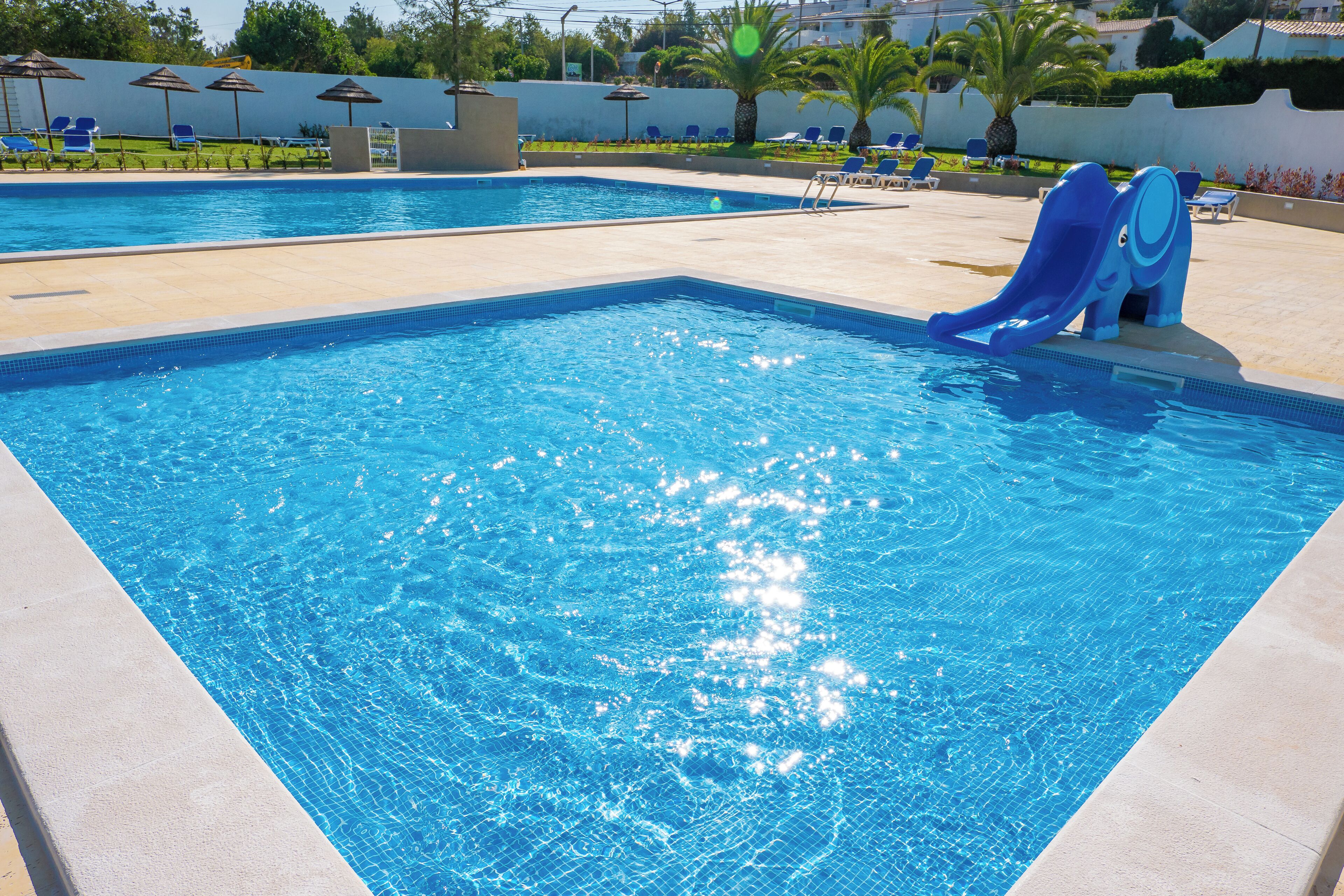 A swimming pool with a slide, lounge chairs, and palm trees.