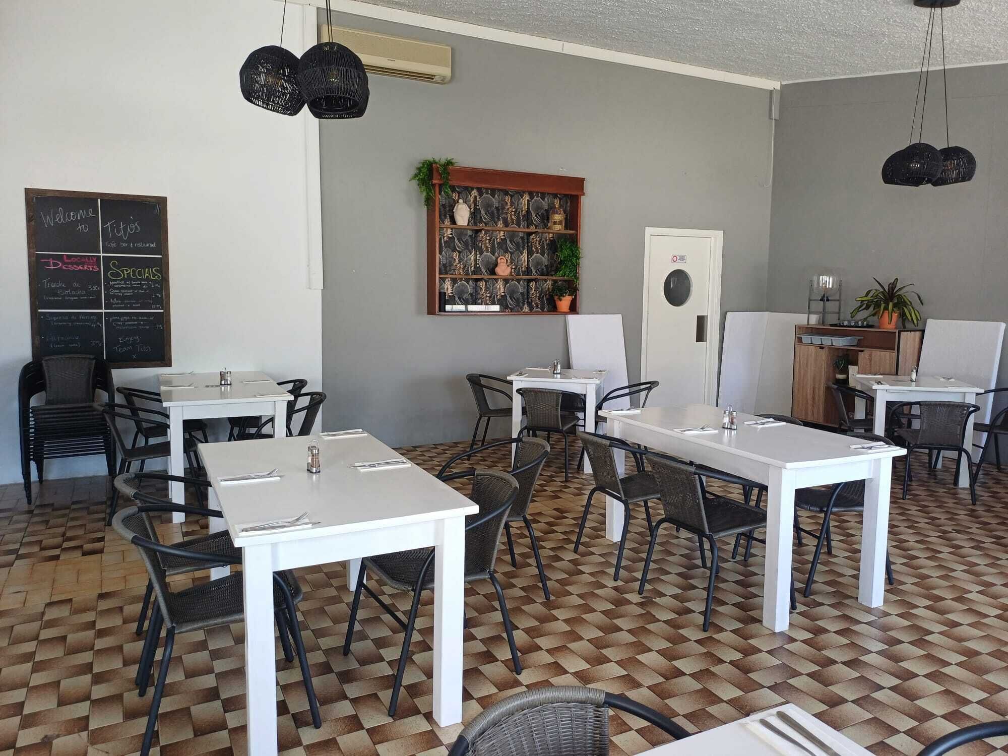 En café med hvide borde og stole, en tavle med menu og en dekorativ væg med et planter.
