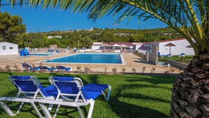 A pool area with blue lounge chairs, a clear blue sky, and a view of houses in the background. - Parque de Campismo Orbitur Valverde (Lagos)