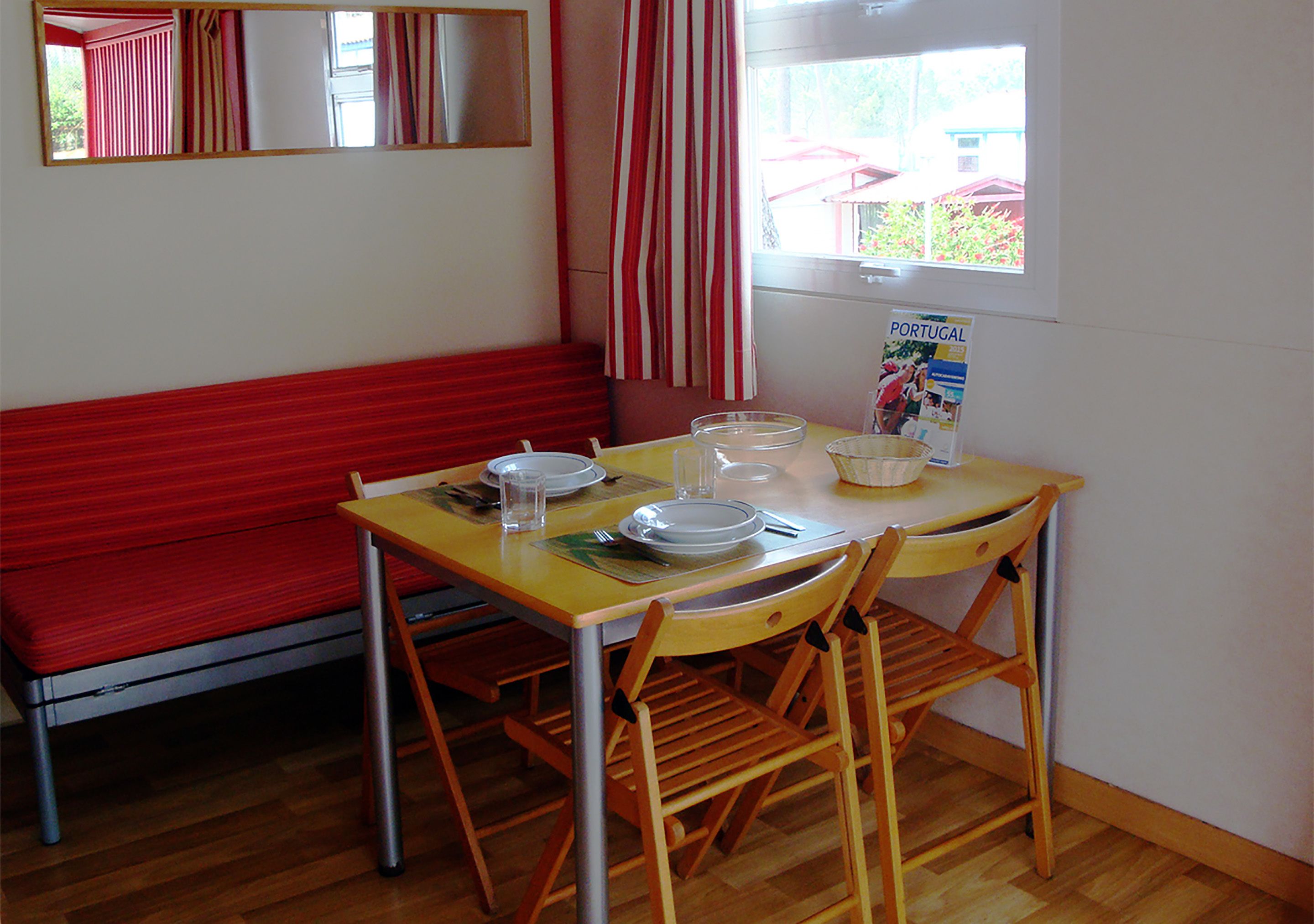 Un'area pranzo con tavolo in legno, quattro sedie, una panca rossa e una finestra con tende.