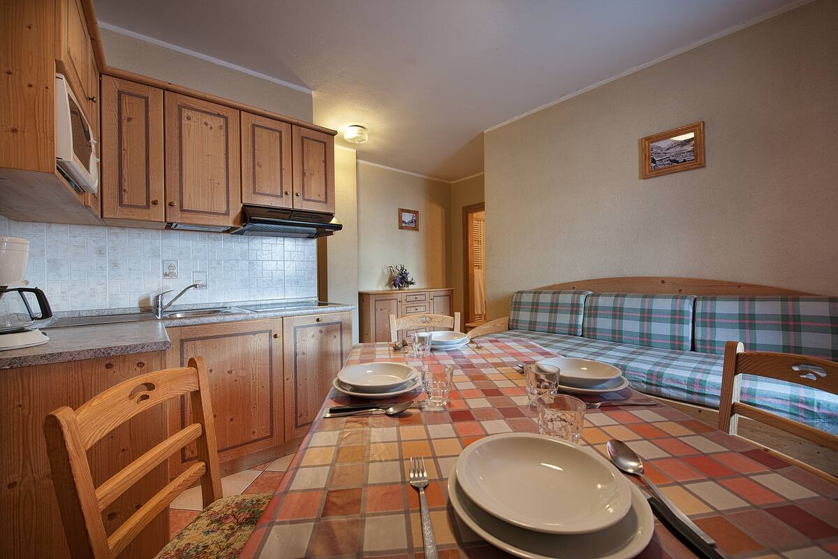 A compact kitchen with wooden cabinets, a tiled backsplash, and a checkered tablecloth.