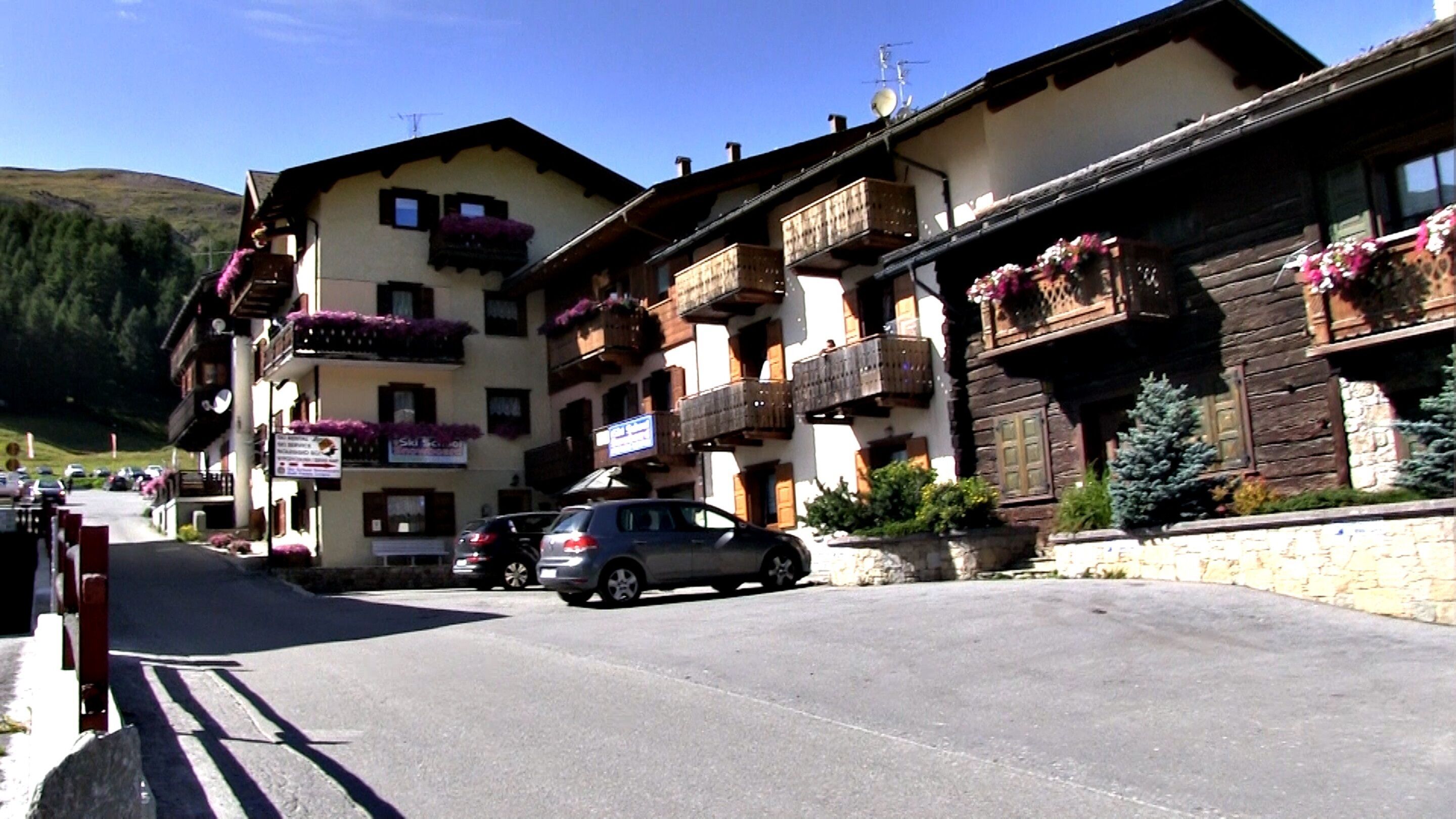 Una calle con edificios europeos tradicionales, incluyendo un hotel con balcones y macetas con flores.