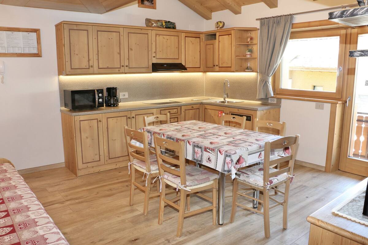 A compact kitchen with wooden cabinets, a dining table with chairs, a microwave, and a coffee maker.