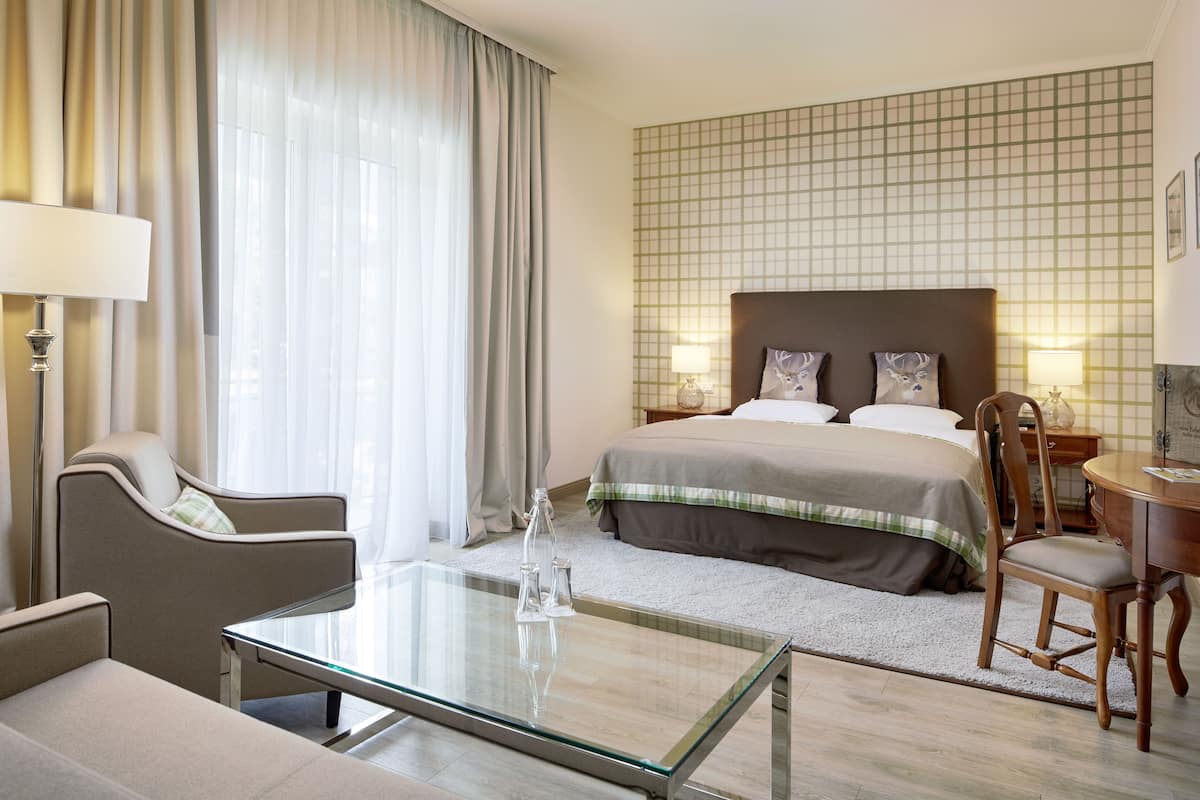 Habitación de hotel con una cama grande, una mesa de centro de vidrio, una silla, un escritorio y una lámpara.