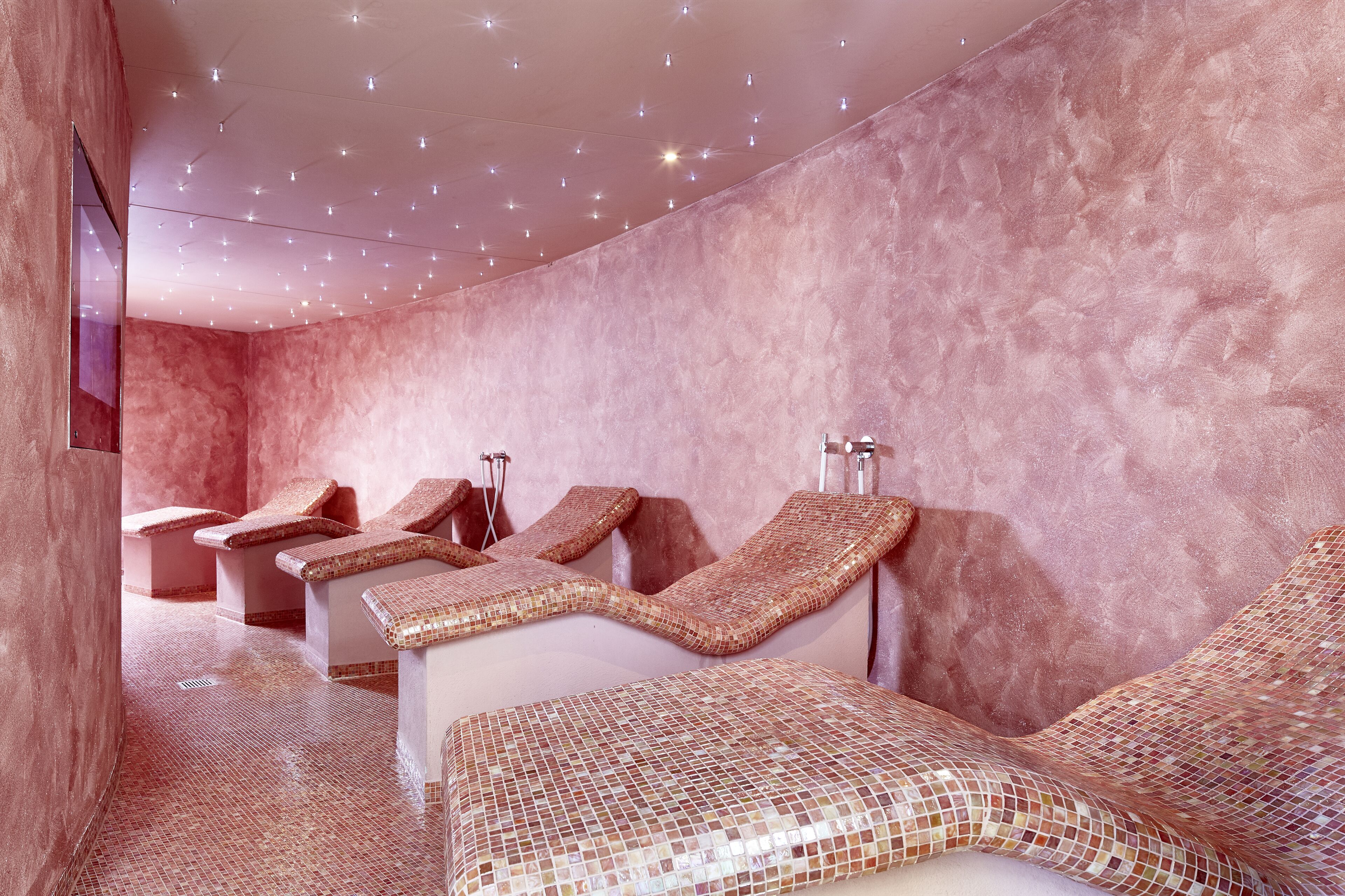 Un cuarto de spa con varias sillas de masaje, piso de baldosas y una pared rosa con textura.