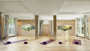 A spacious room with wooden flooring, large windows, and yoga mats with purple cushions. - Das Alpenhaus Gasteinertal (Bad Hofgastein)