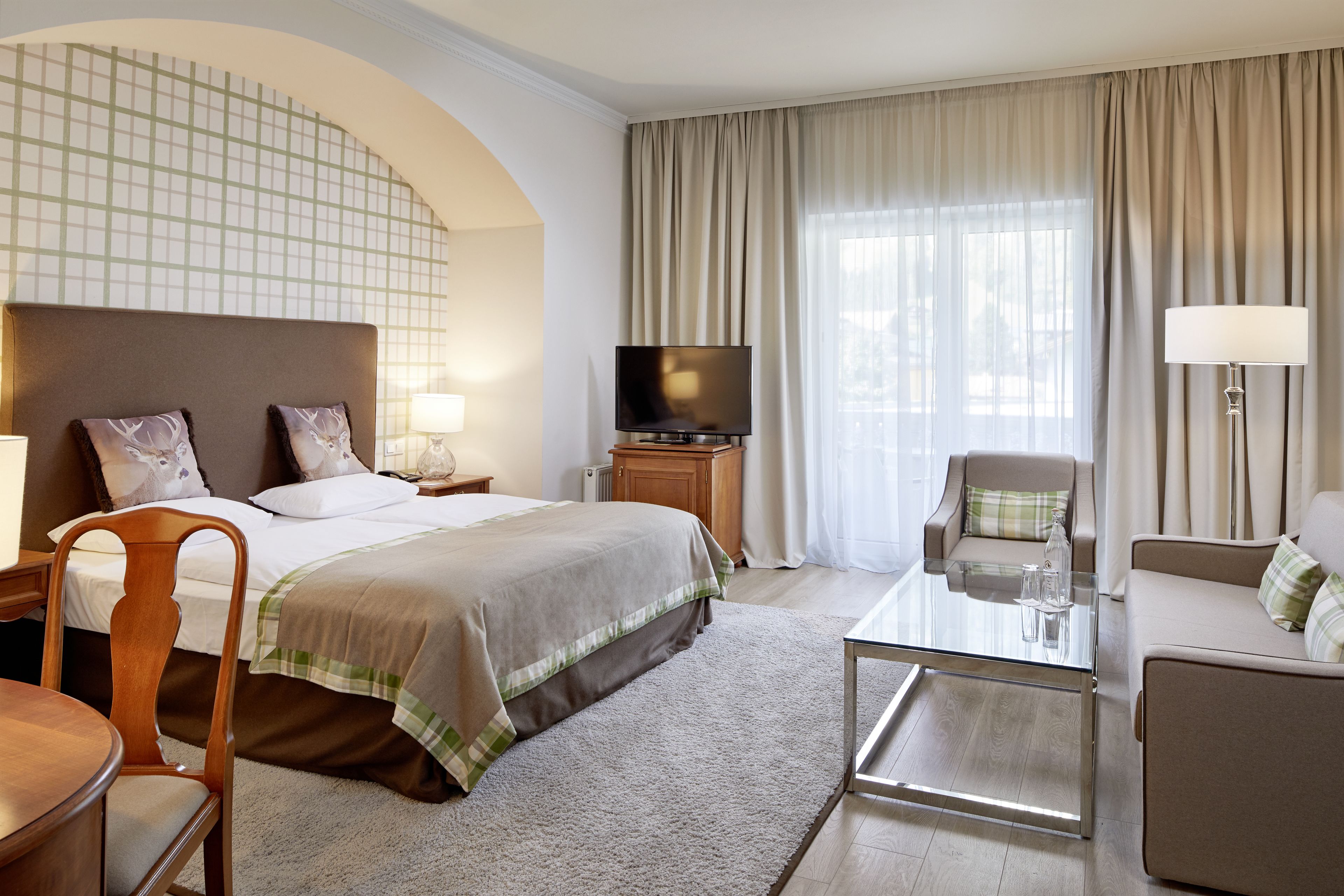 Habitación de hotel con cama, televisión, sofá, sillón, mesa y lámpara.