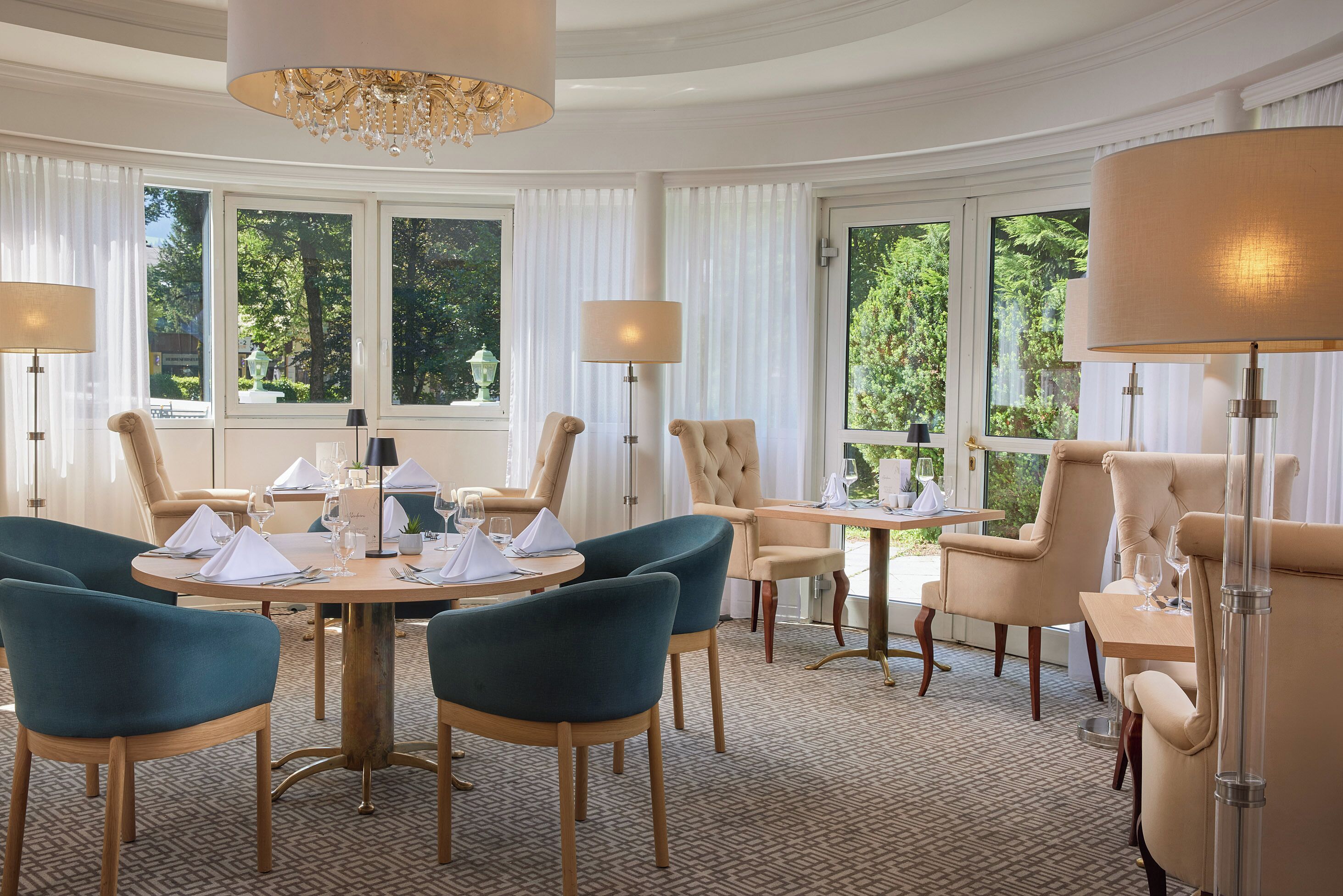 A dining area with round tables, upholstered chairs, and chandeliers.