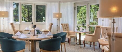 A dining area with round tables, upholstered chairs, and chandeliers.