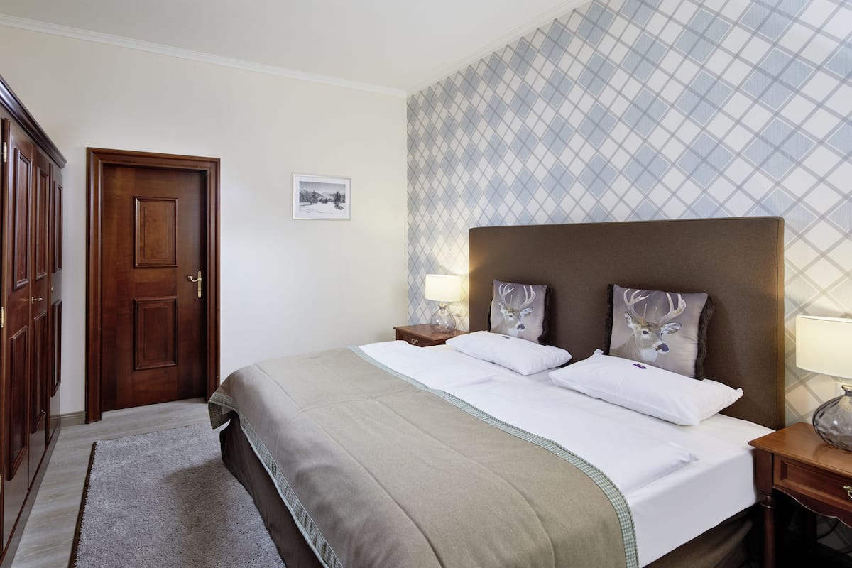 Una habitación de hotel con una cama grande, dos mesitas de noche, un armario de madera y un papel tapiz estampado.