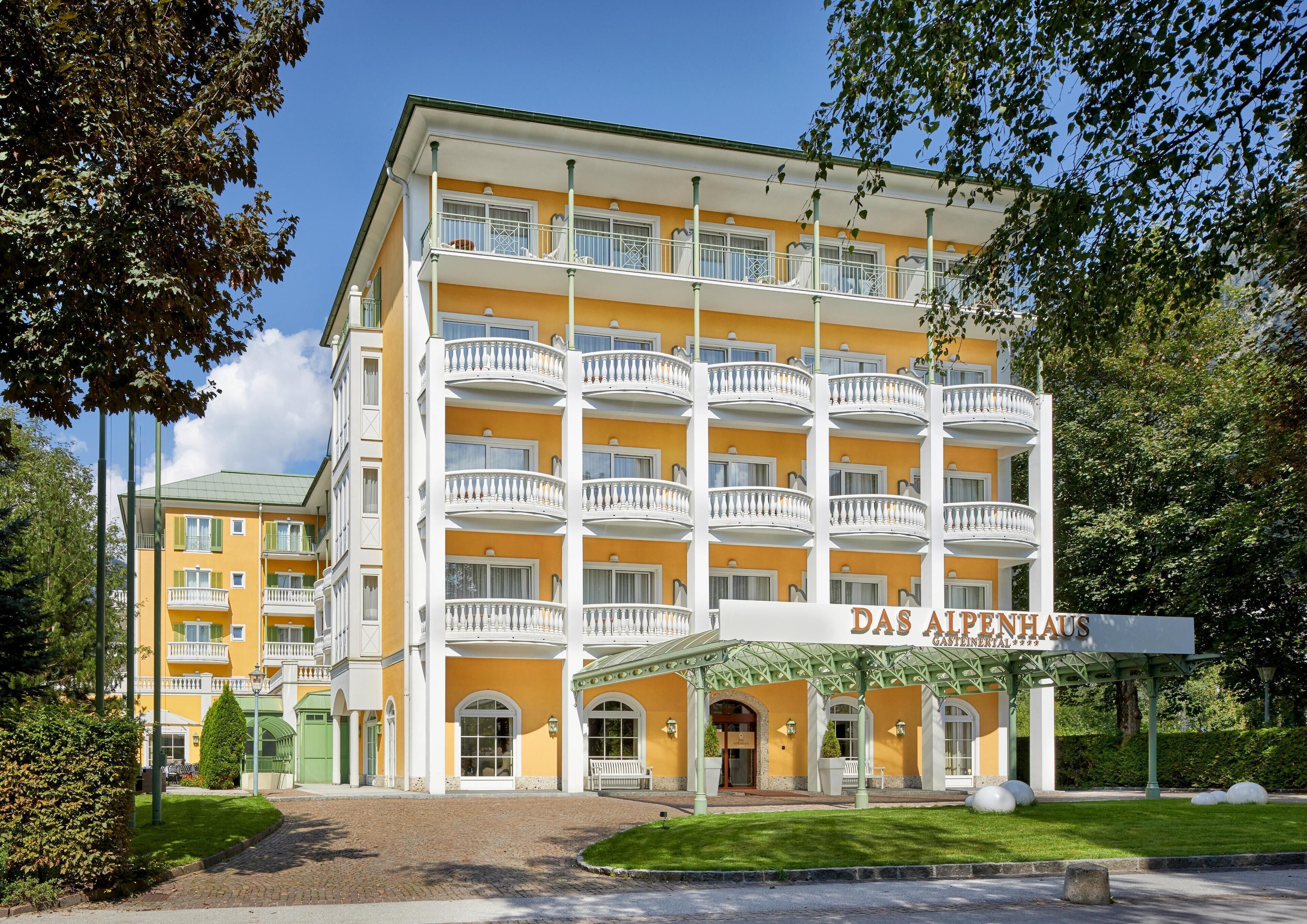 Un hotel de varios pisos con fachada amarilla, múltiples balcones y un letrero que dice "Das Alpenhaus".