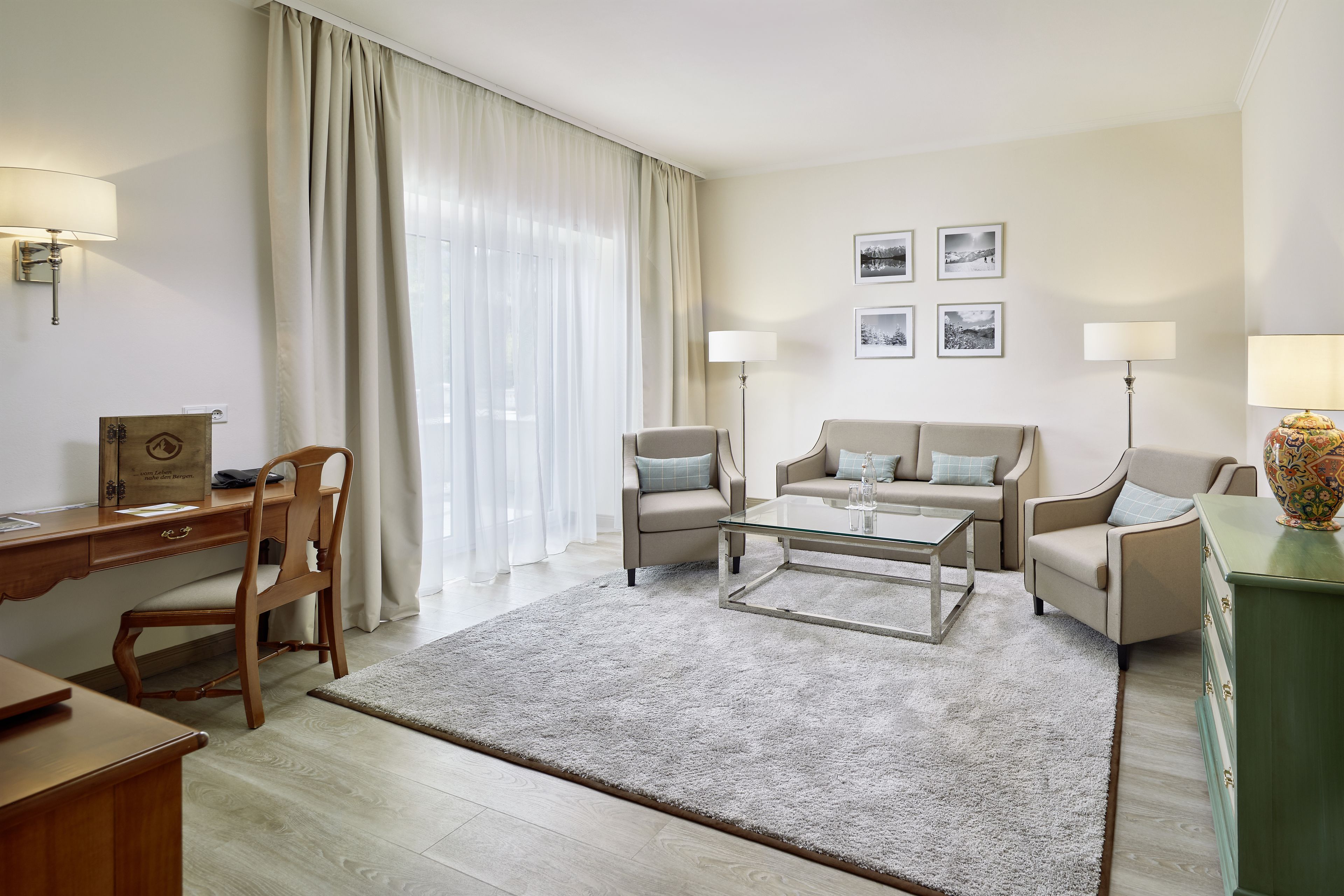 Ein Hotelzimmer mit Schreibtisch aus Holz, zwei Sesseln, einer Couch, einem Glastisch und einem grünen Schrank.