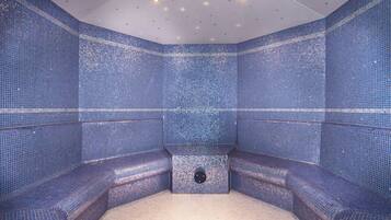 A room with blue mosaic walls, a central seating area, and a ceiling with recessed lighting.