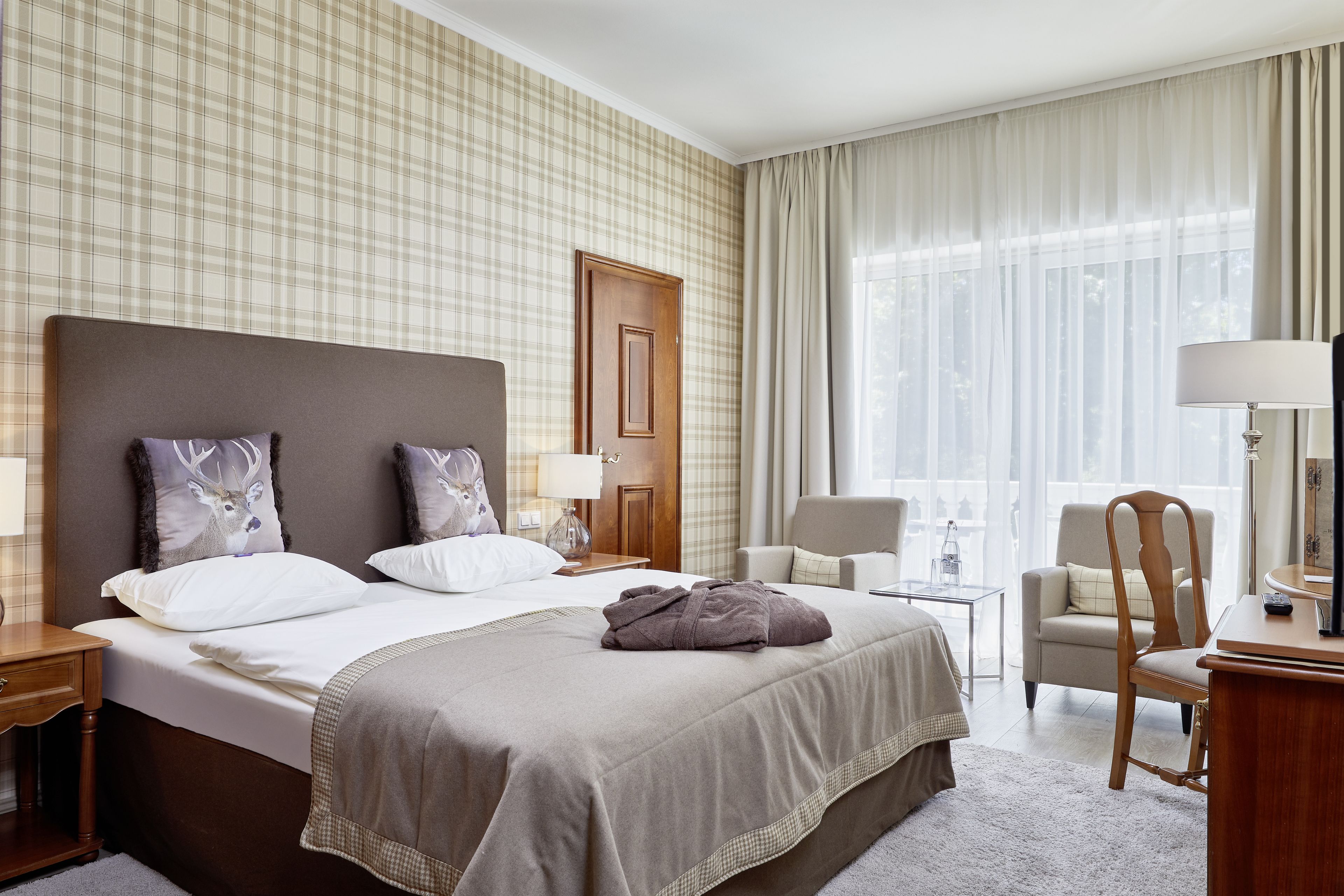 Una habitación de hotel con una cama grande, dos sillones, un escritorio y una ventana con cortinas.