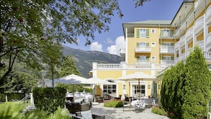 A hotel courtyard with outdoor seating, umbrellas, and a mountain backdrop. - Das Alpenhaus Gasteinertal (Bad Hofgastein)