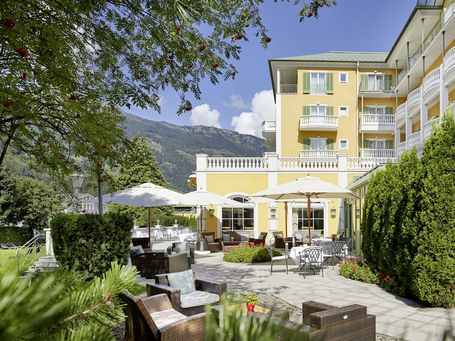 Une cour d’hôtel avec des espaces de détente en plein air, des parasols et une vue sur les montagnes en arrière-plan.