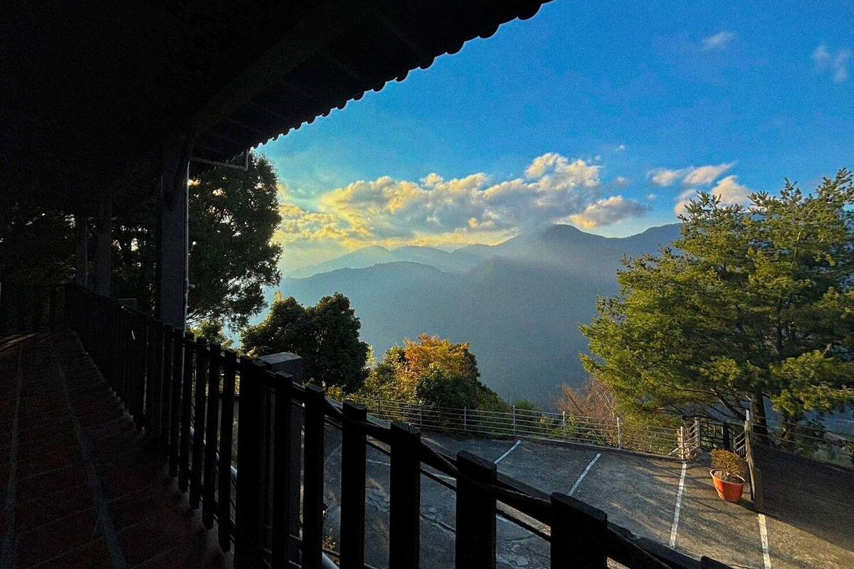A view from a covered balcony overlooking a mountainous landscape with trees and a clear sky.