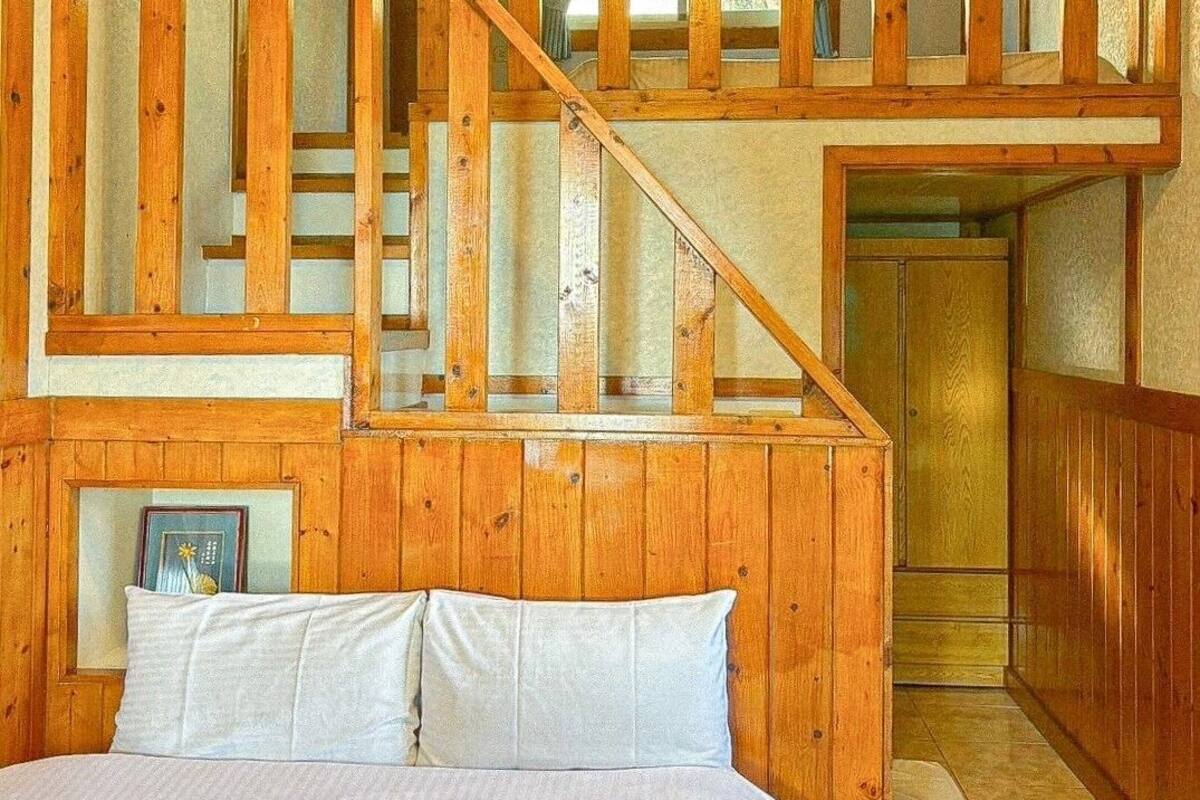 A bedroom with a large bed, wooden staircase, and a view of the outside.