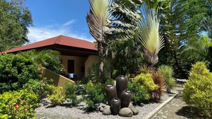A building with a red roof, surrounded by tropical plants and a stone pathway. - Alona Swiss Resort (Panglao)