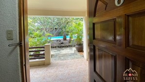 A wooden door with the number 6, leading to a tiled patio with a pool and potted plants. - Alona Swiss Resort (Panglao)