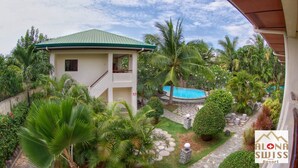 A resort with a pool, lush greenery, and a two-story building with a green roof. - Alona Swiss Resort (Panglao)