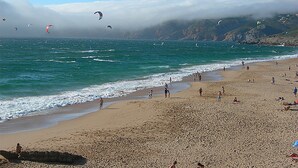 Una playa con gente, cometas y un litoral rocoso.