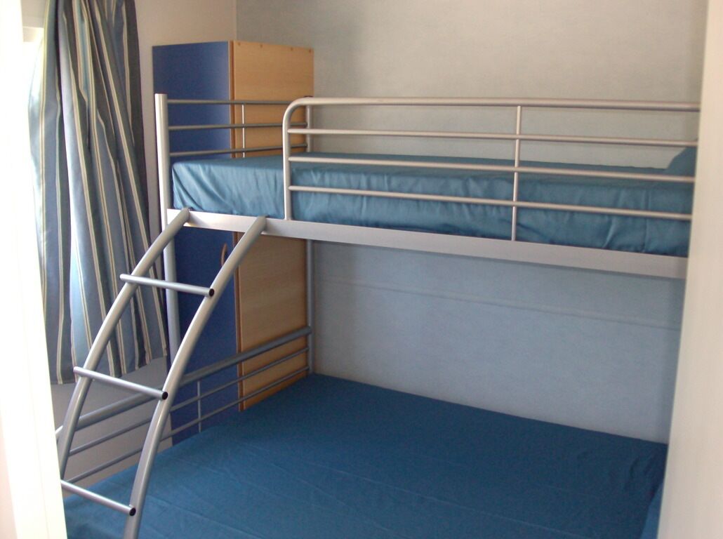 A bunk bed room with a ladder, a blue mattress, and a wooden cabinet.