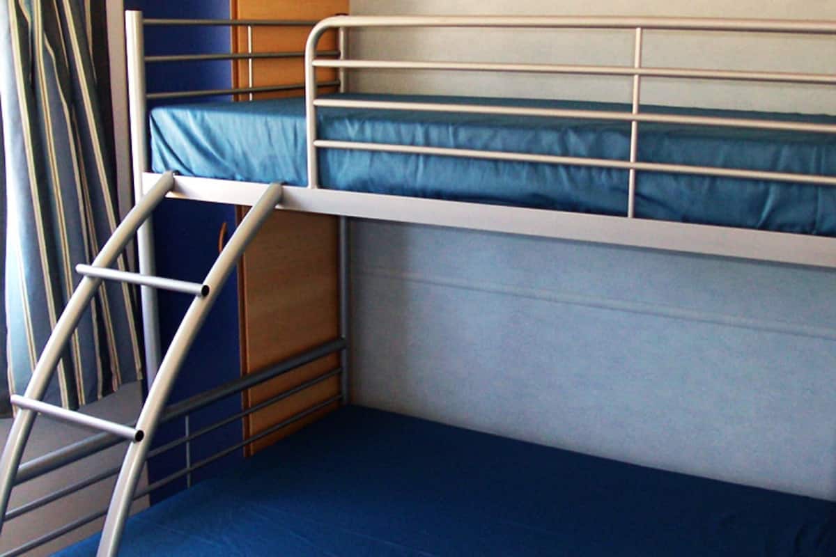 A bunk bed with a ladder, a wooden side table, and a blue mattress.